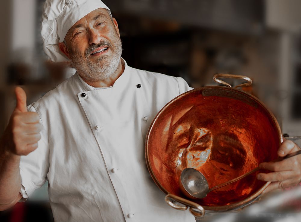 Businessfotografie, Business Projects. Chef in white uniform displays a copper bowl with thumbs up gesture.