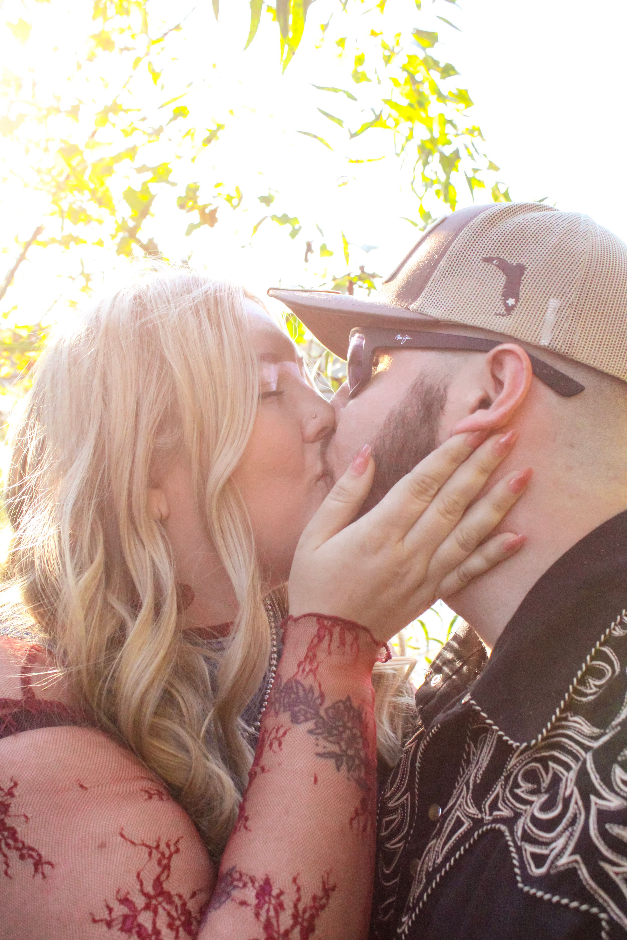 Couple sharing romantic moment in sunlit outdoor setting with artistic golden lighting.