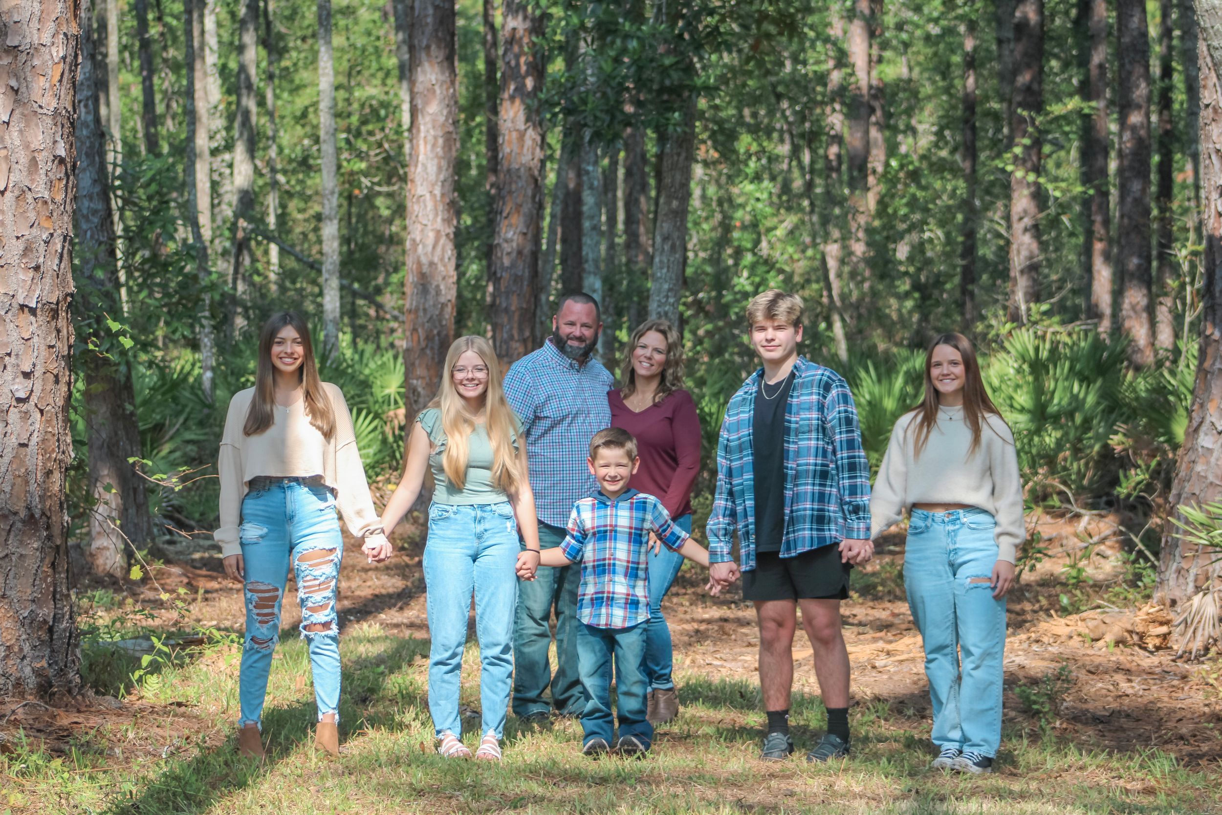 Extended family group posing casually together in wooded outdoor setting.