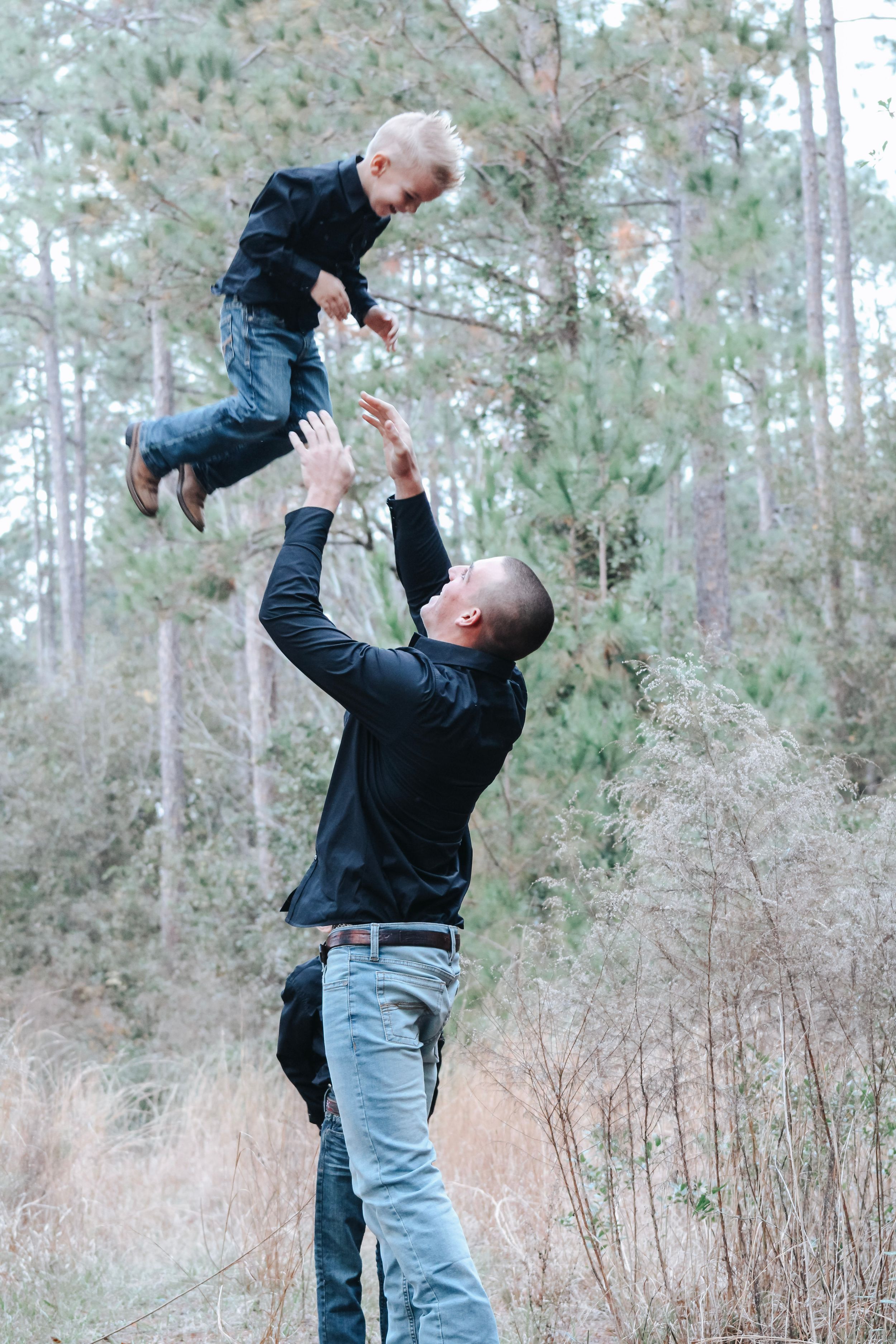 Parent and child playing together outdoors with joyful lifting sequence in wooded area.