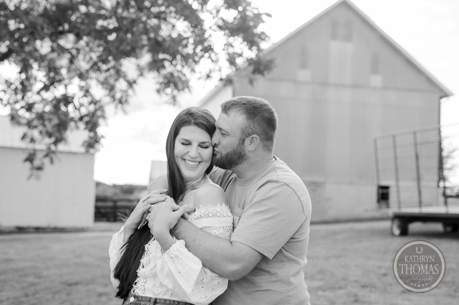 Black and white portrait of couple sharing intimate moment in front of rustic barn.