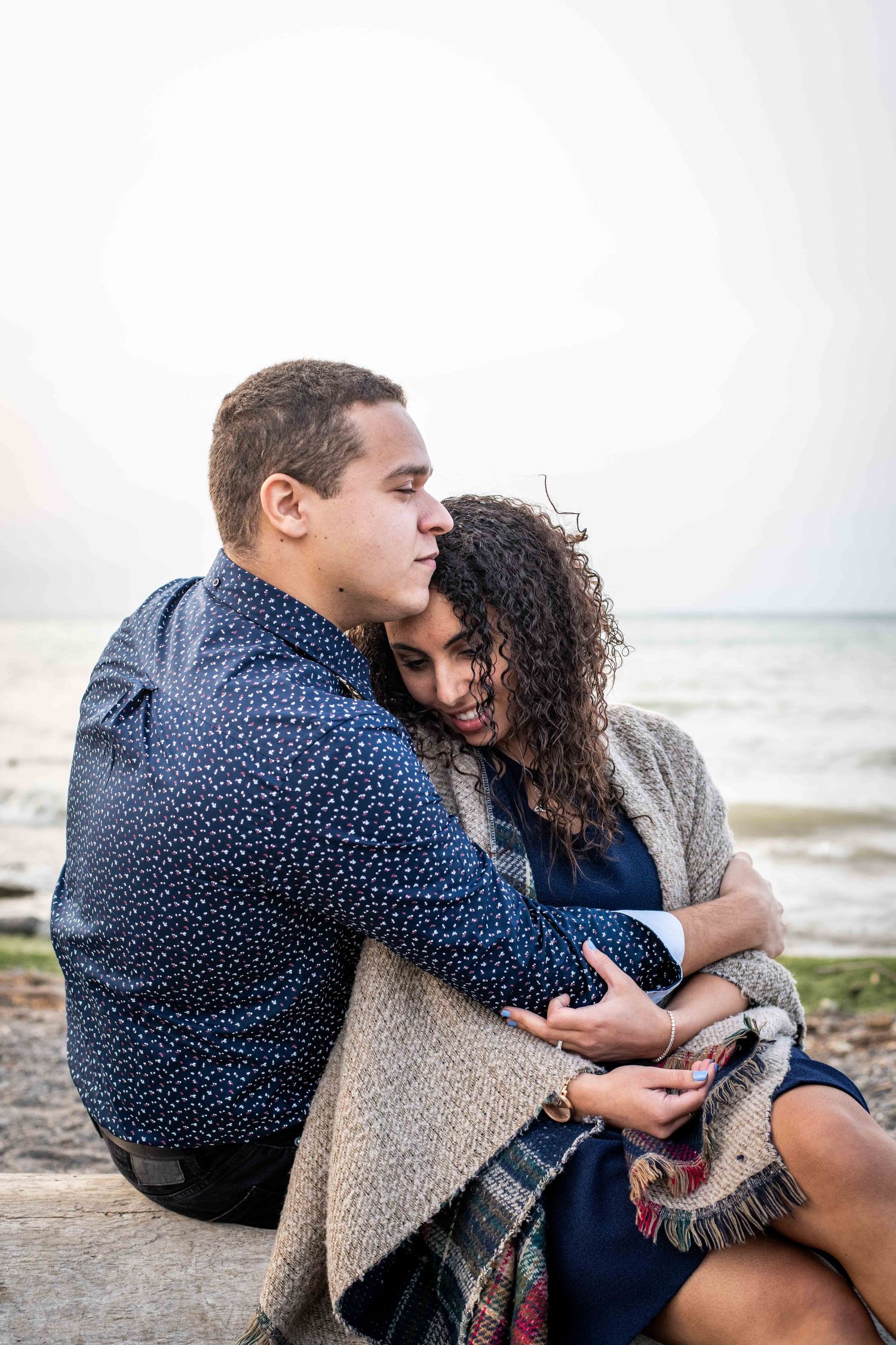 An intimate seaside moment with cozy sweaters and a blanket wrap on a cloudy day.