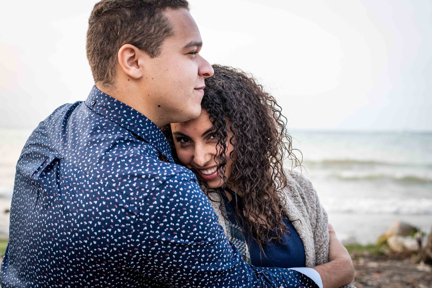 A romantic beachside portrait capturing a warm embrace against the lakeside backdrop.