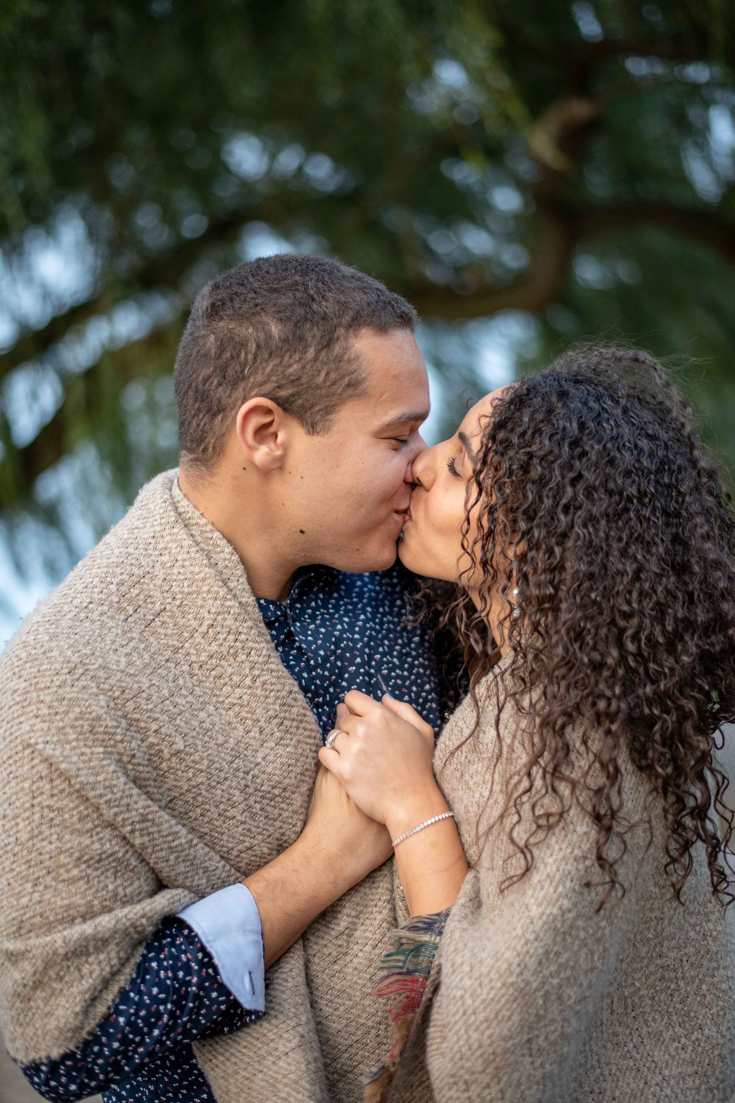 A romantic moment shared under pine trees wrapped in cozy neutral-toned blankets.