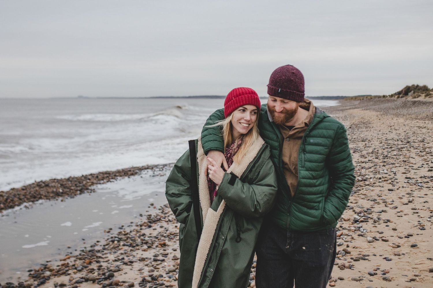 Couple in winter coats sharing intimate moment on cold beach.