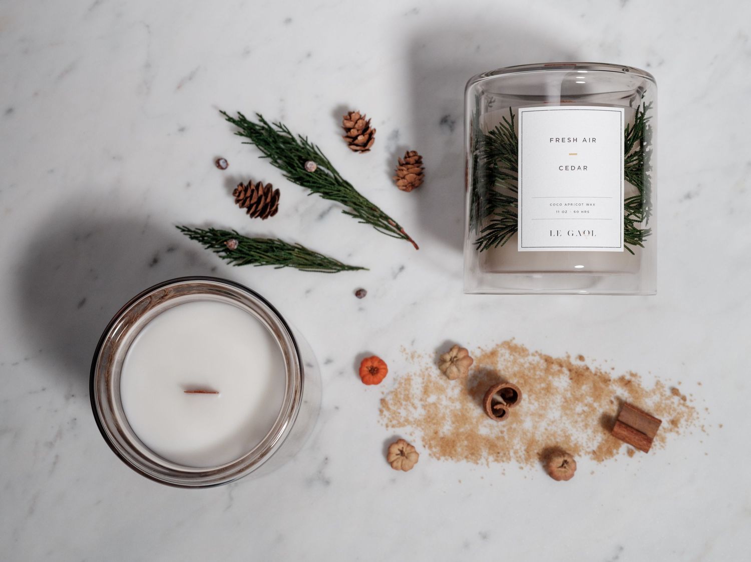 Minimalist candle arrangement with pine sprigs and bath salts on marble surface.