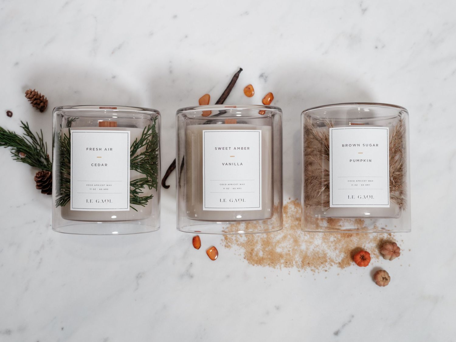 Three glass candle vessels arranged with pine sprigs and decorative elements on white marble.