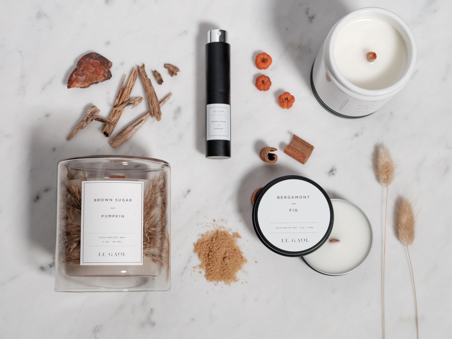 Luxury beauty product flatlay with candles, wooden elements and spices on marble surface.