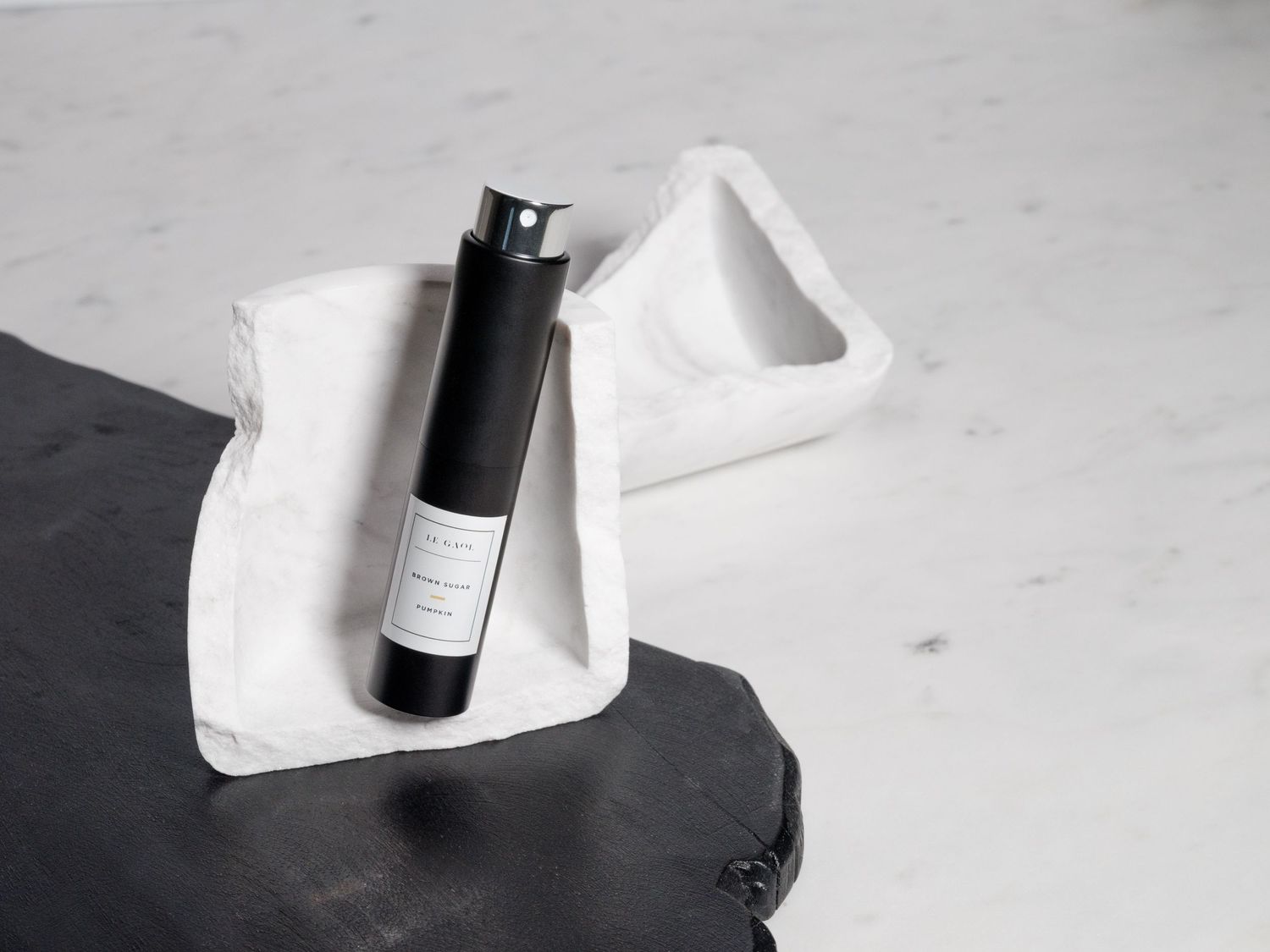 Black minimalist bottle with white label displayed on white cloth against dark background.