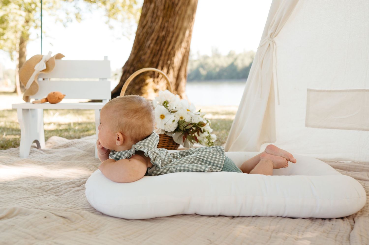 White pregnancy pillow with floral bouquet in outdoor bohemian setting with tent and tree.
