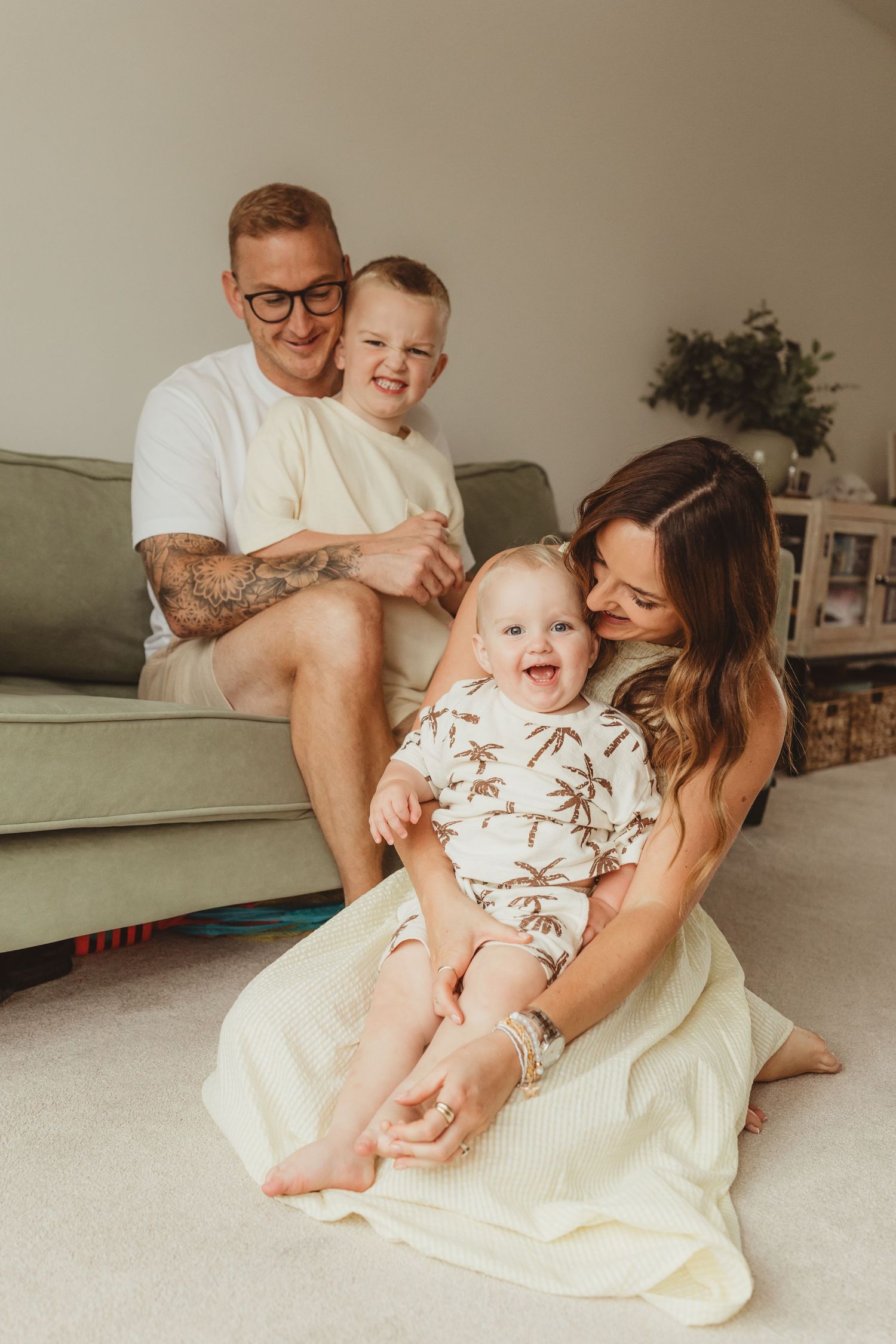 A family relaxes together on a white bed in a cozy bedroom with natural lighting and minimalist decor.