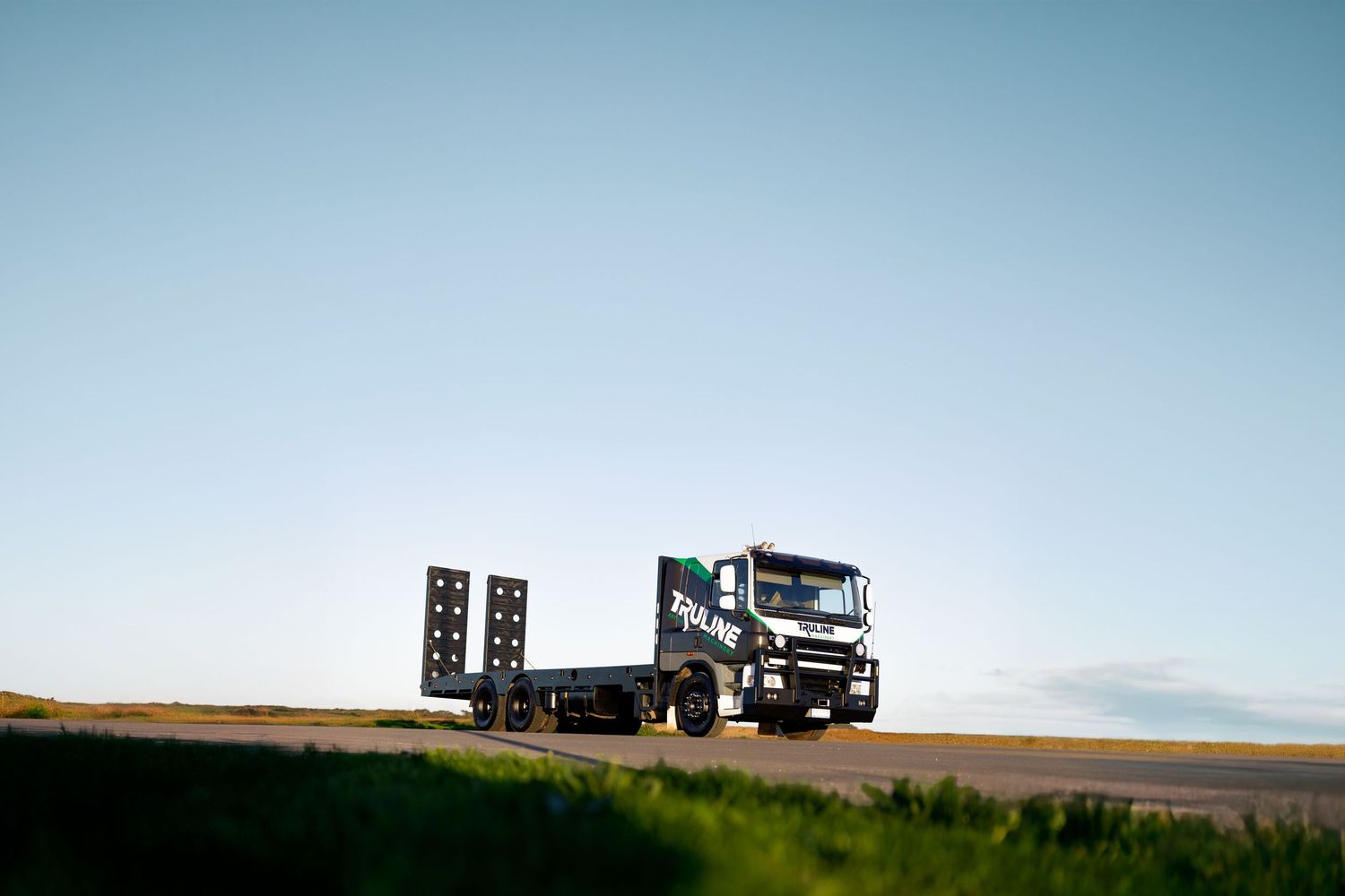 A black transport truck silhouetted against blue sky on rolling hills.