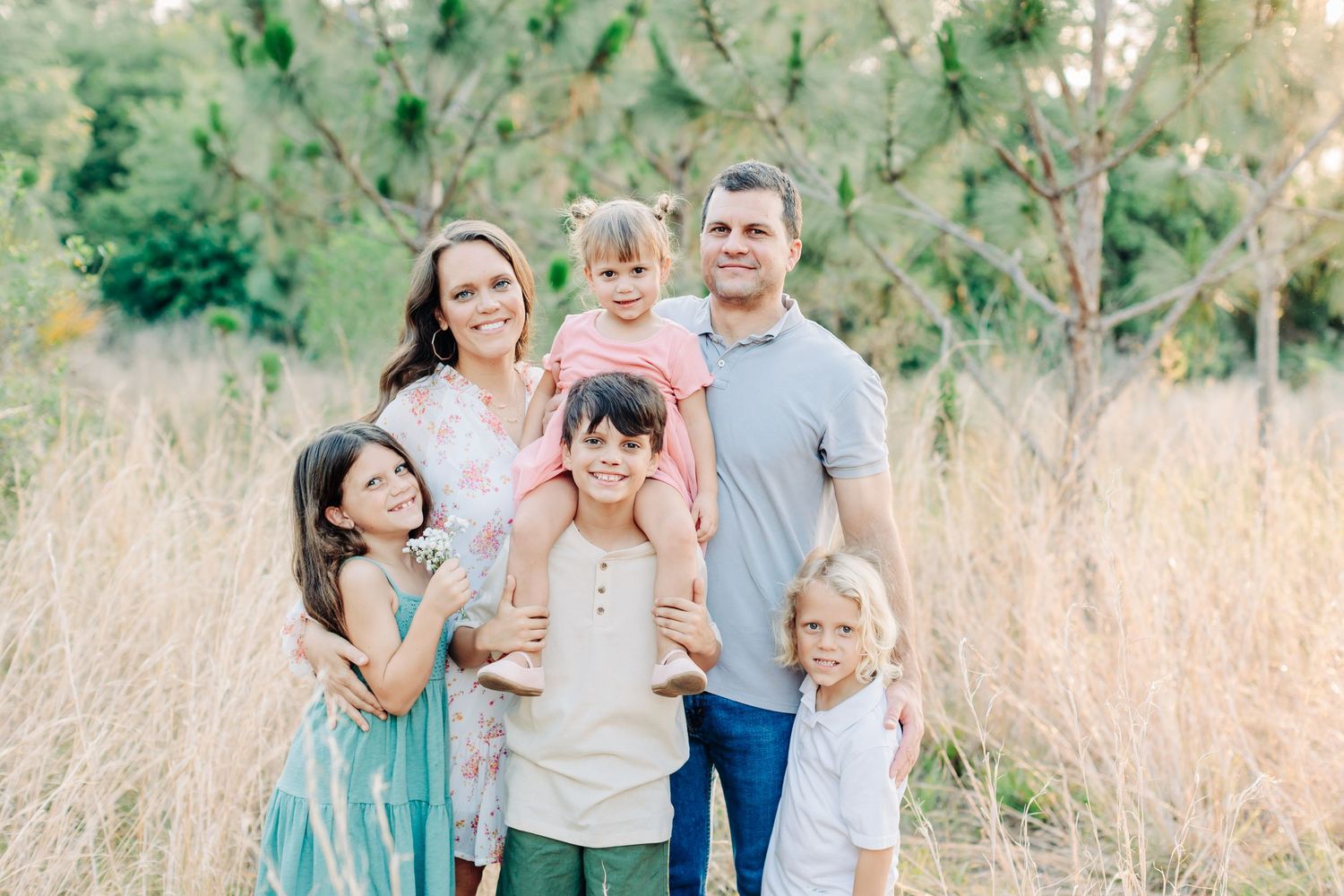 Family piled up smiling and looking at the camera in the field with tall grass