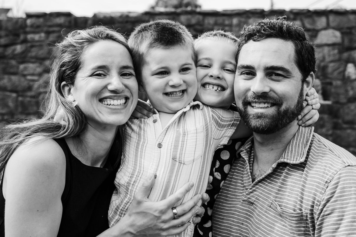 A multi-generational family stands together smiling on a wooden boardwalk in a lush forest setting.