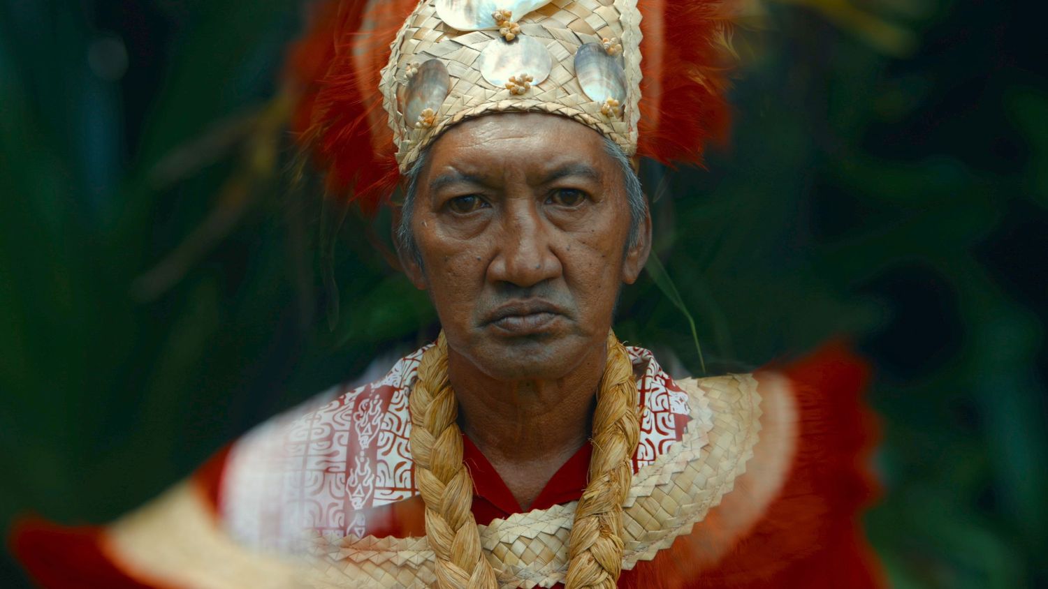 A person wearing ornate gold traditional Indonesian ceremonial clothing and headdress with red feathers.