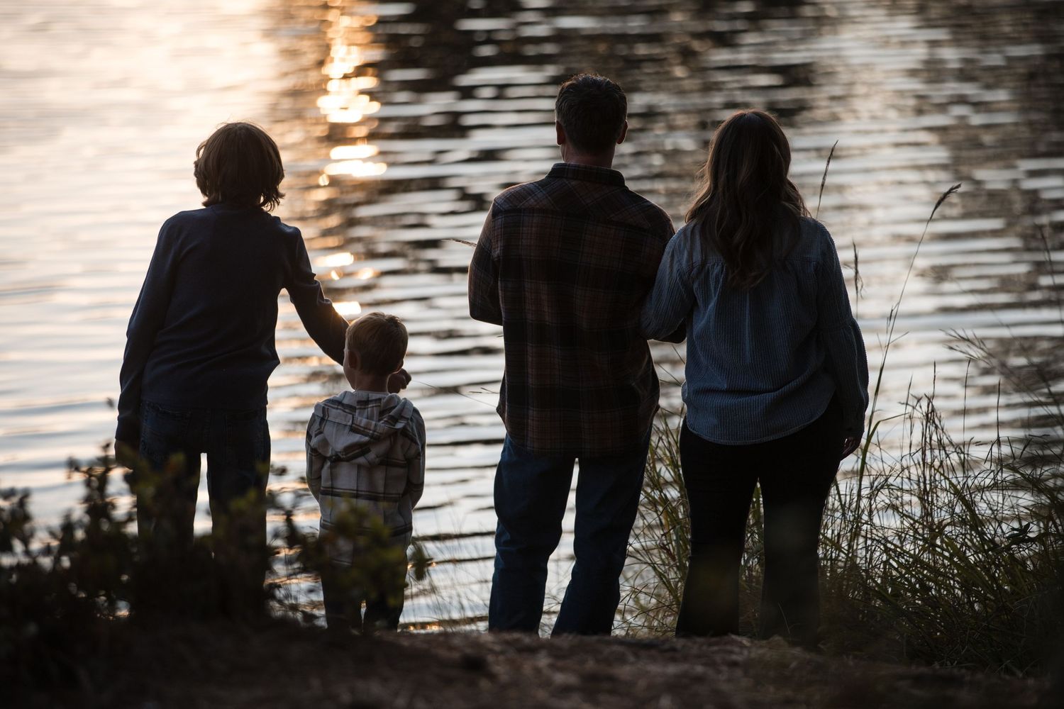 Silhouettes of a family standing together at sunset by a lake watching the light reflect off the water's surface.