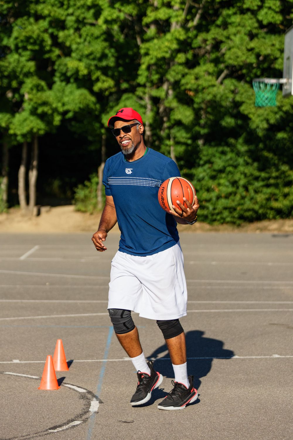 Basketball player in casual sportswear practicing on an outdoor court on a sunny day.