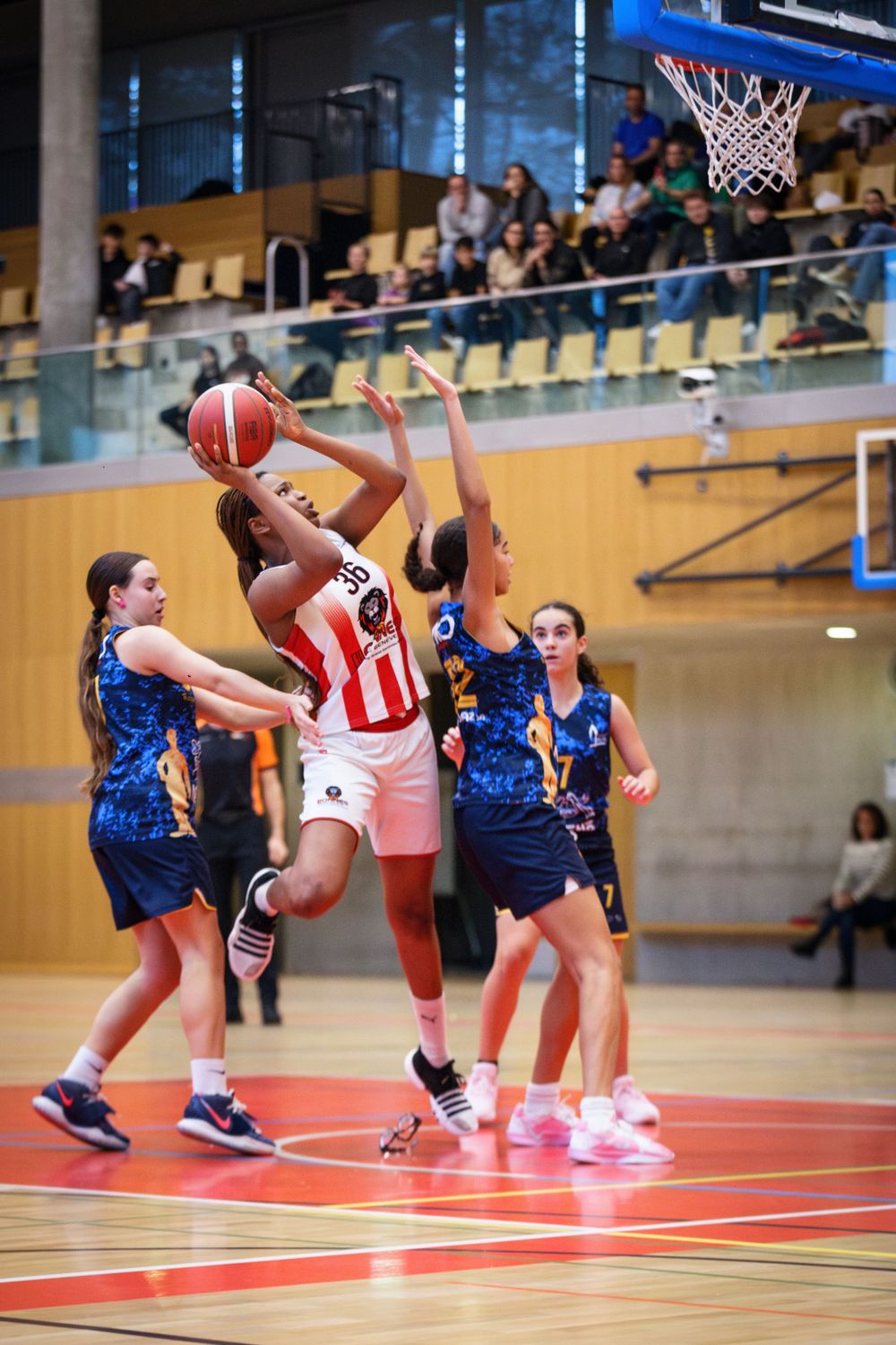 Women's basketball game showing player in striped uniform attempting shot against defenders.