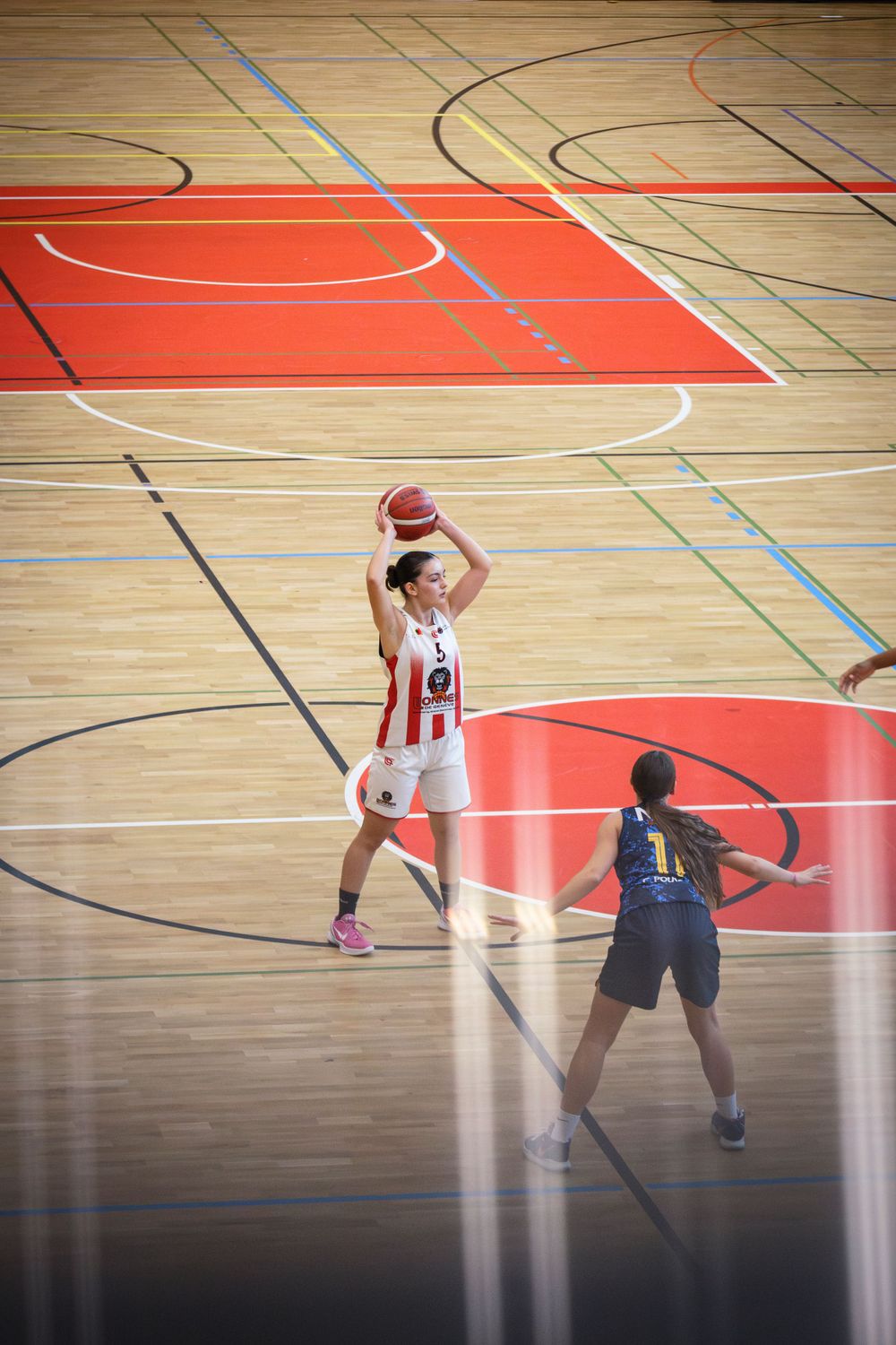 Basketball players compete on indoor court with distinct red center circle marking.