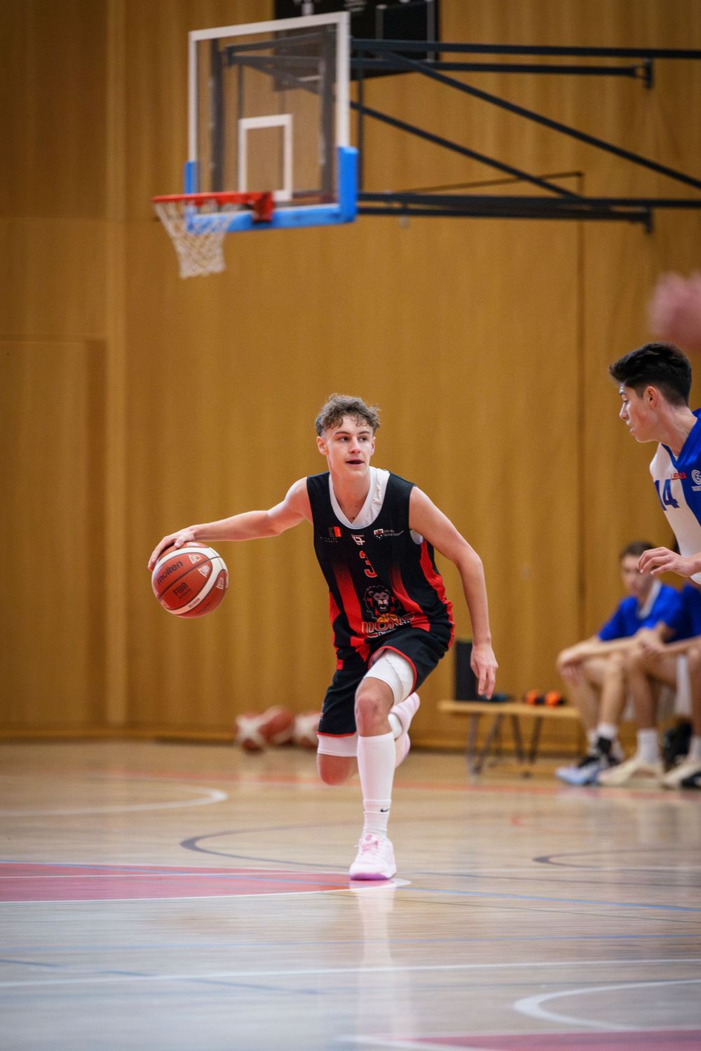 Basketball player in a red and black uniform dribbles on an indoor court.
