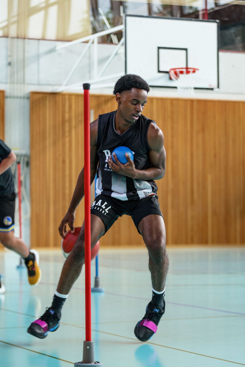 Basketball player in black Ball Academy uniform performs agility training drill.