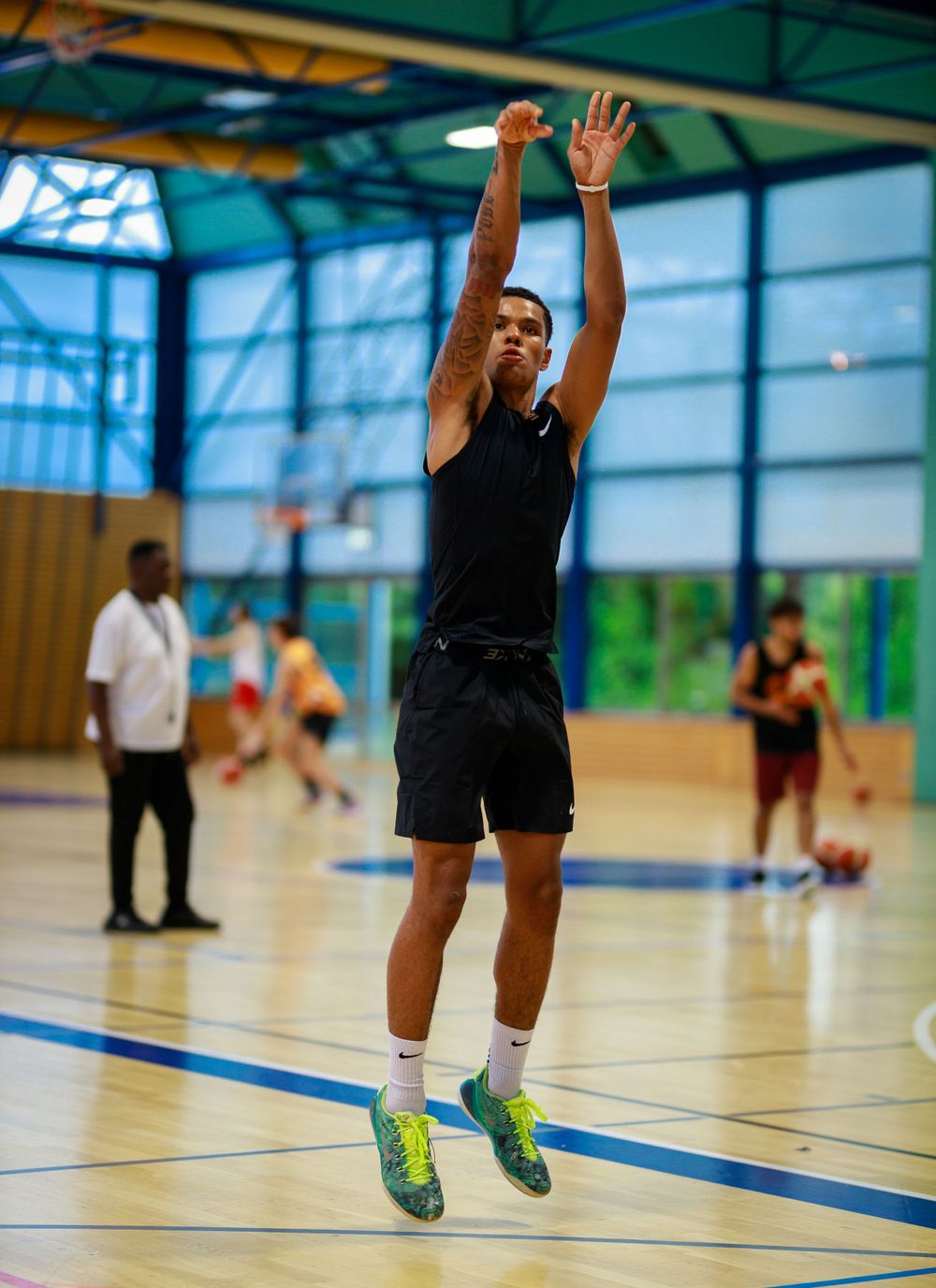 Player takes jump shot on indoor basketball court wearing black athletic attire.