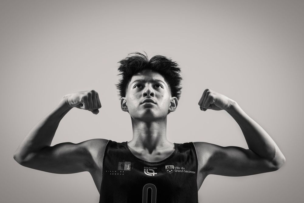 Athletic player in black jersey poses with raised fists against grey background.