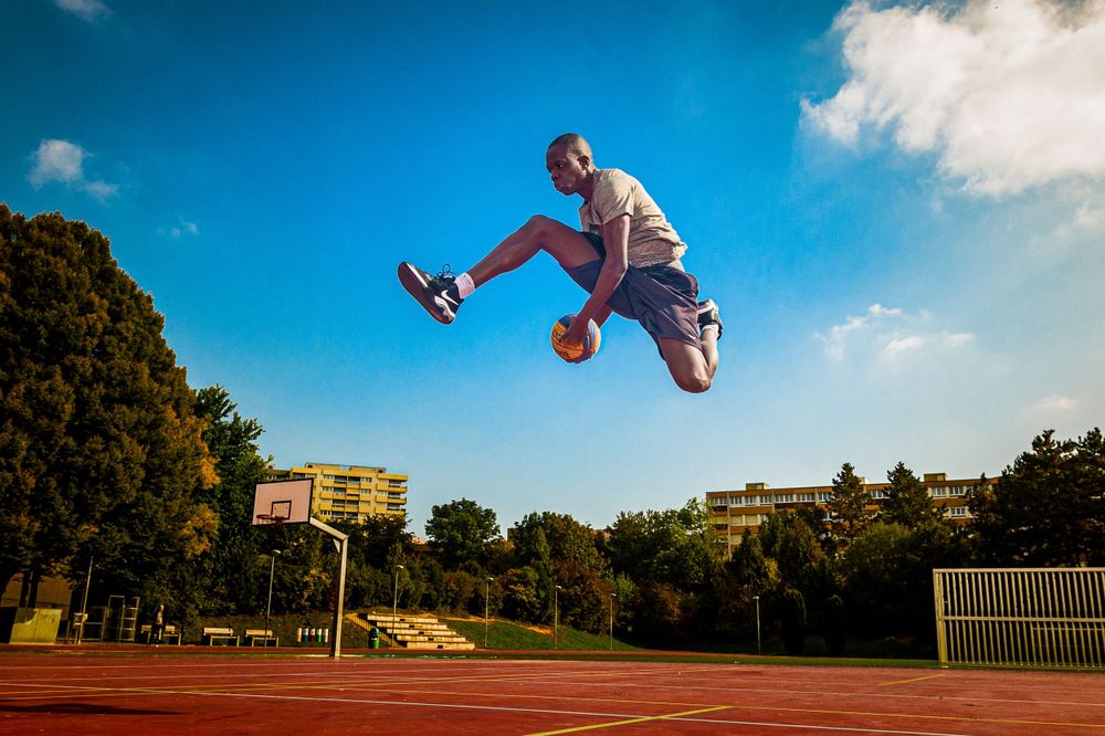 Athletic figure performing acrobatic jump on outdoor track field against blue sky.