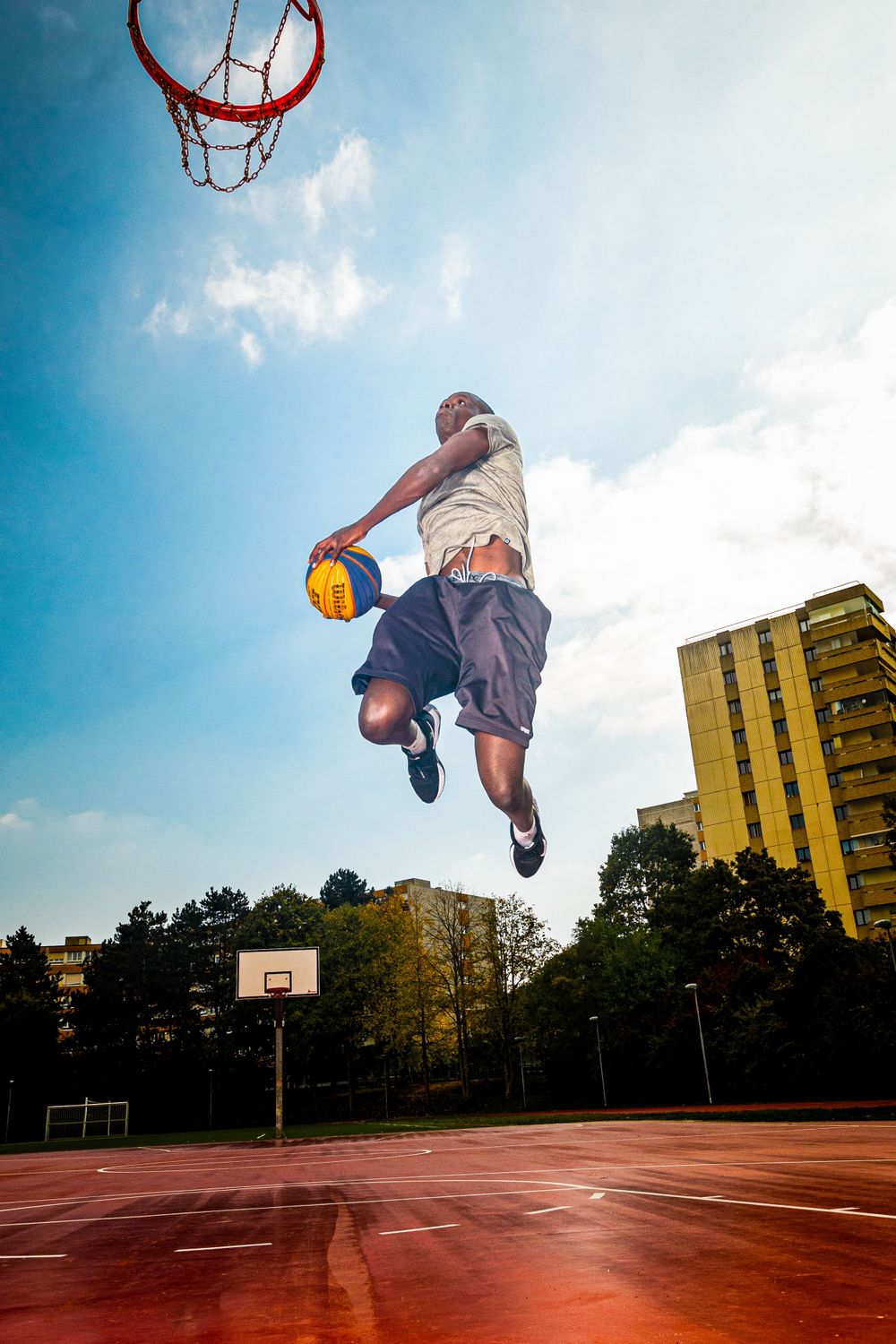 Basketball player soars for dramatic dunk against bright blue sky on outdoor court.