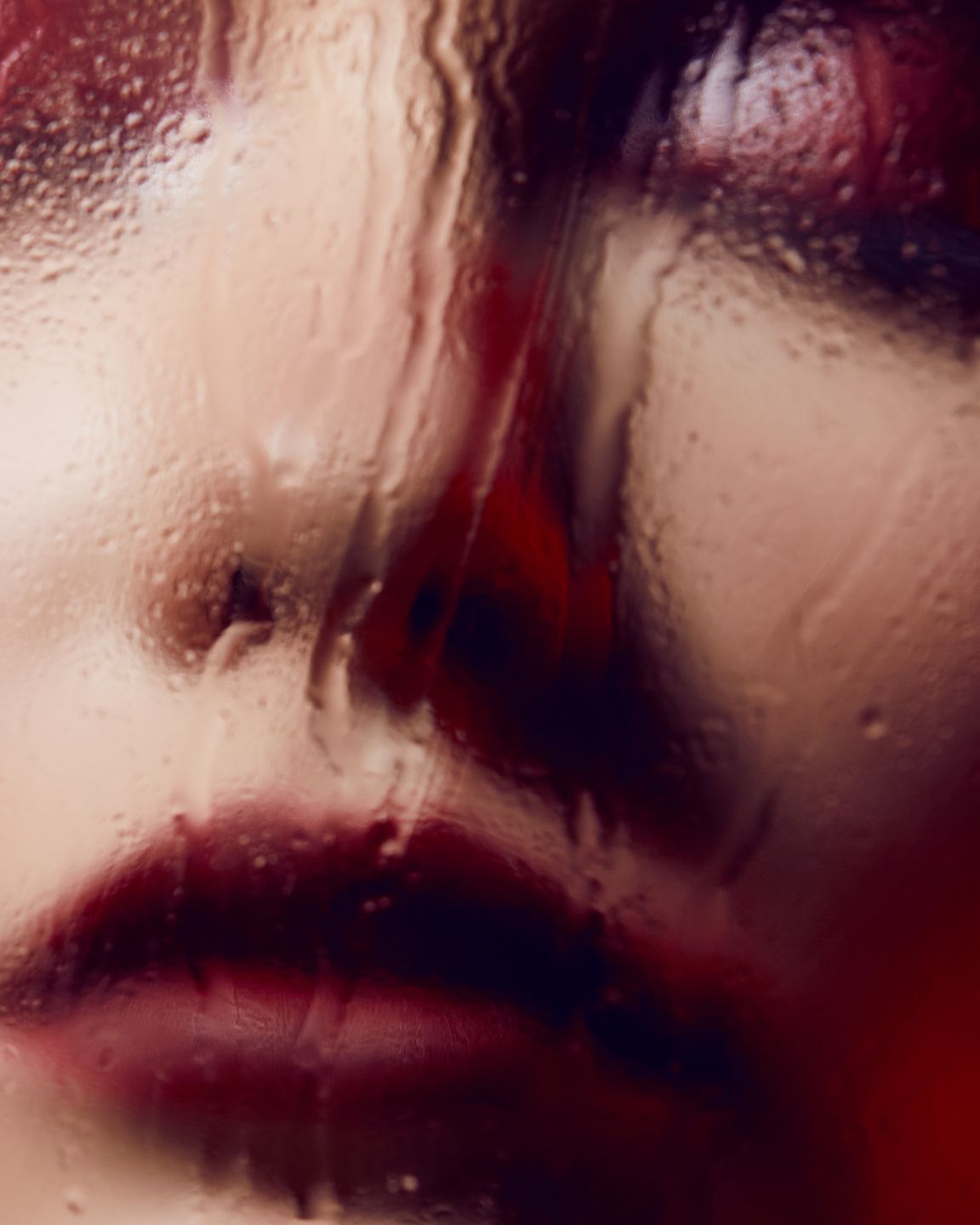 Close up artistic portrait showing red lips and water droplets on glass creating a dreamy effect.