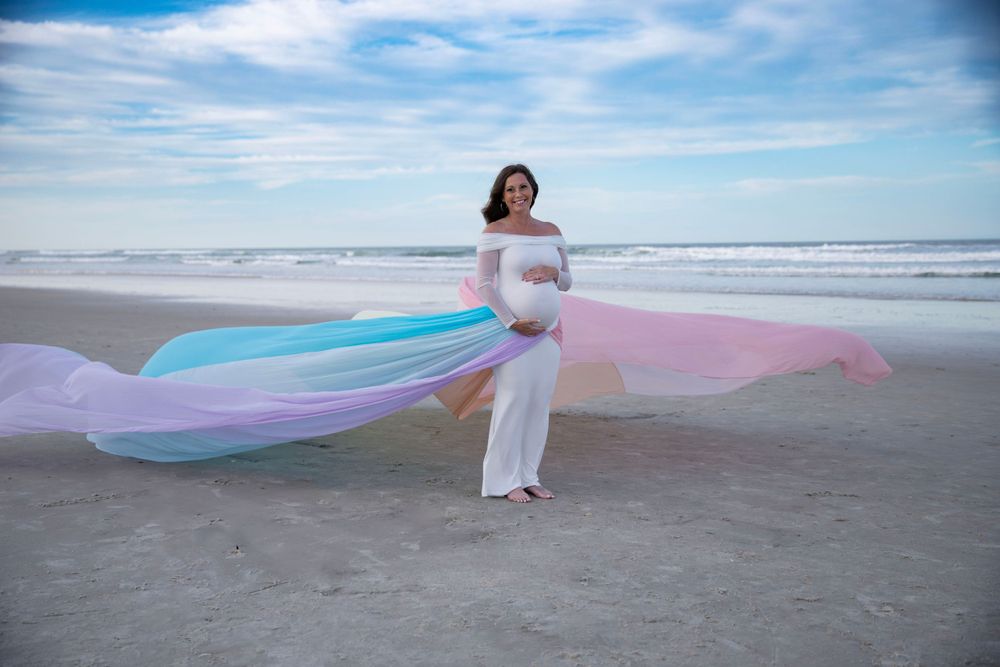Pregnant woman on beach with flowing fabric during outdoor maternity photography session in Florida.