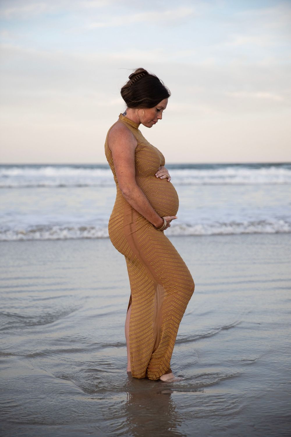 Pregnant woman standing in ocean during sunset outdoor maternity photography session in Florida.