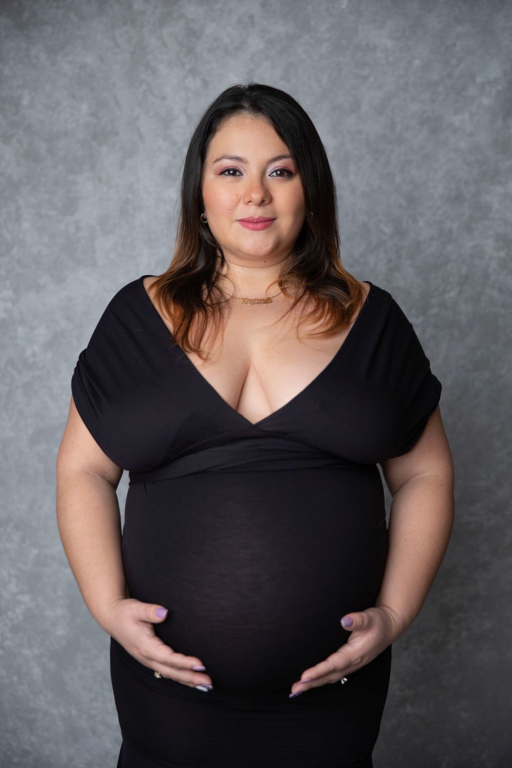 Pregnant woman in black dress cradling baby bump during studio maternity session.