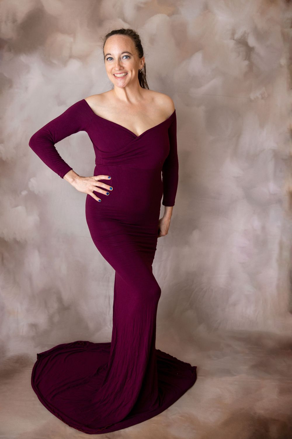 Smiling pregnant woman in form-fitting burgundy off-shoulder maternity gown during Central Florida maternity photography session.