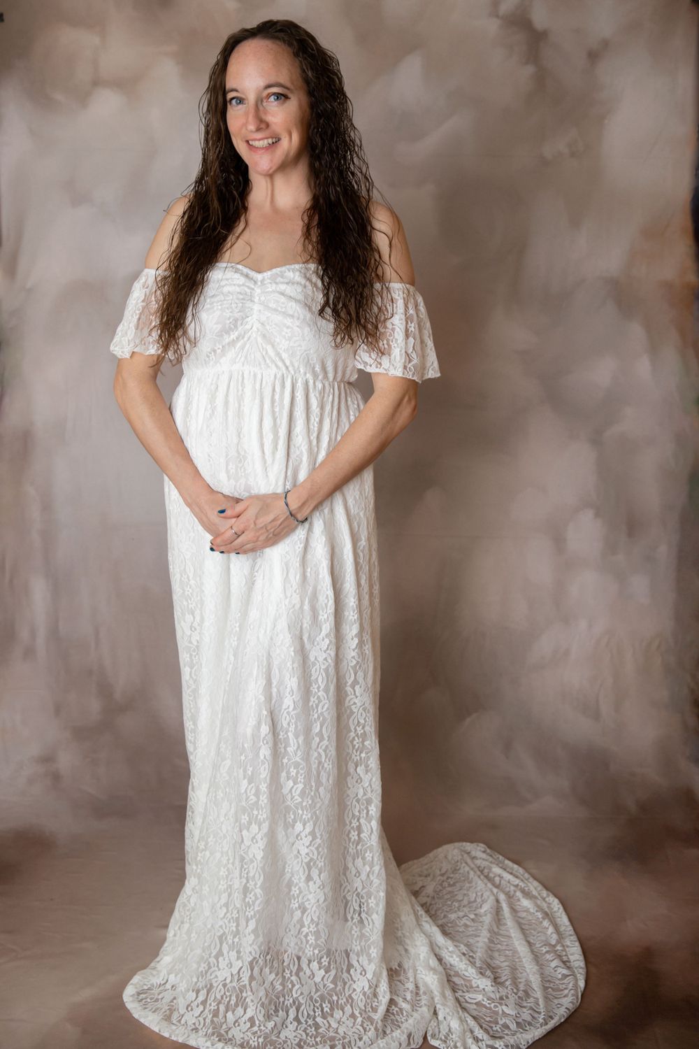 Pregnant woman in off-shoulder white lace gown during studio maternity session.
