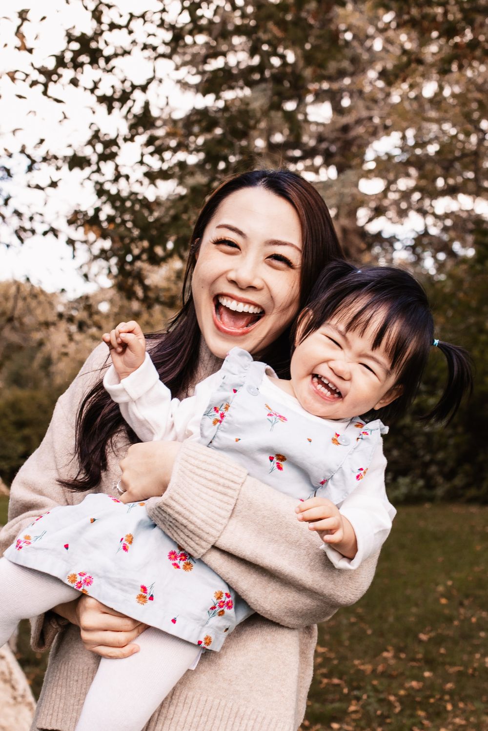 A joyful mother and daughter laughing together outdoors while wearing matching floral dresses in an autumn setting.