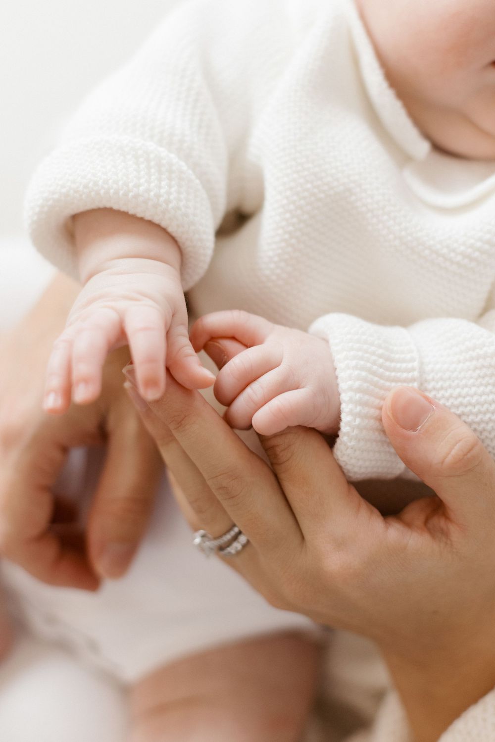 Close-up of a tiny baby's hand gently grasping an adult's finger while wearing a soft white knit garment.