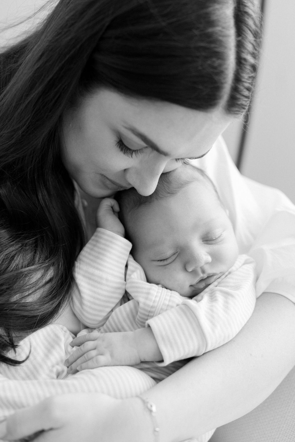 A tender black and white photograph showing a mother tenderly holding her sleeping newborn baby in white clothing.
