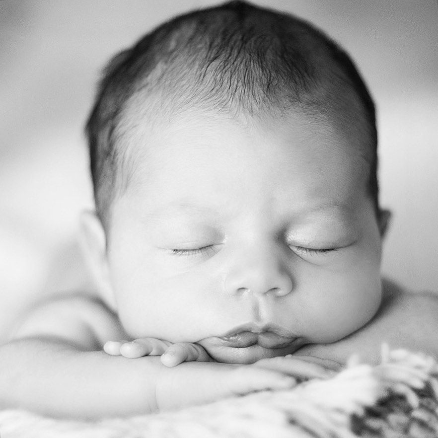 Black and white portrait of a peaceful sleeping newborn baby resting with hands under face.