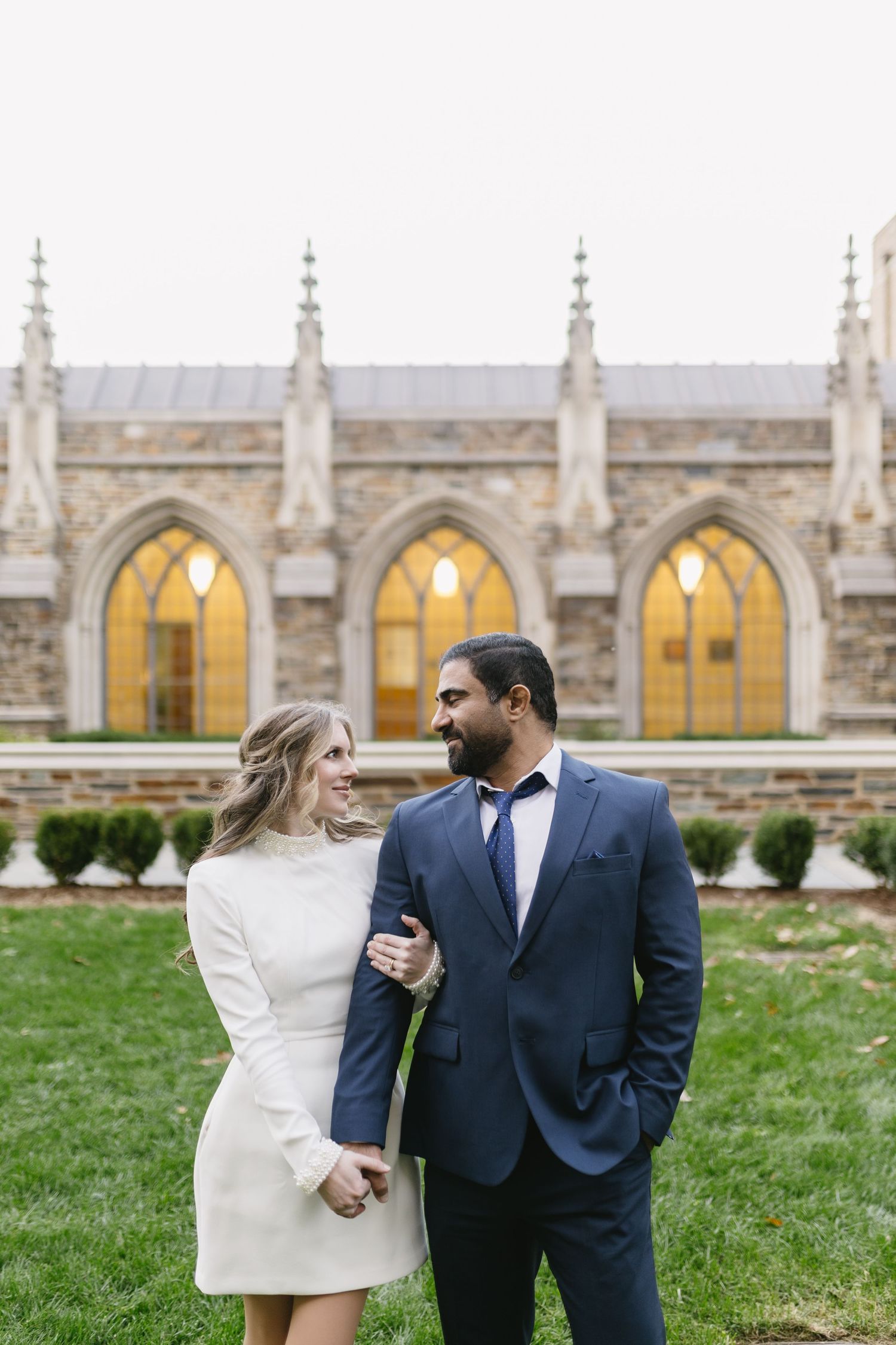 A couple shares a romantic moment in front of a Gothic cathedral with ornate arched windows and stone architecture.