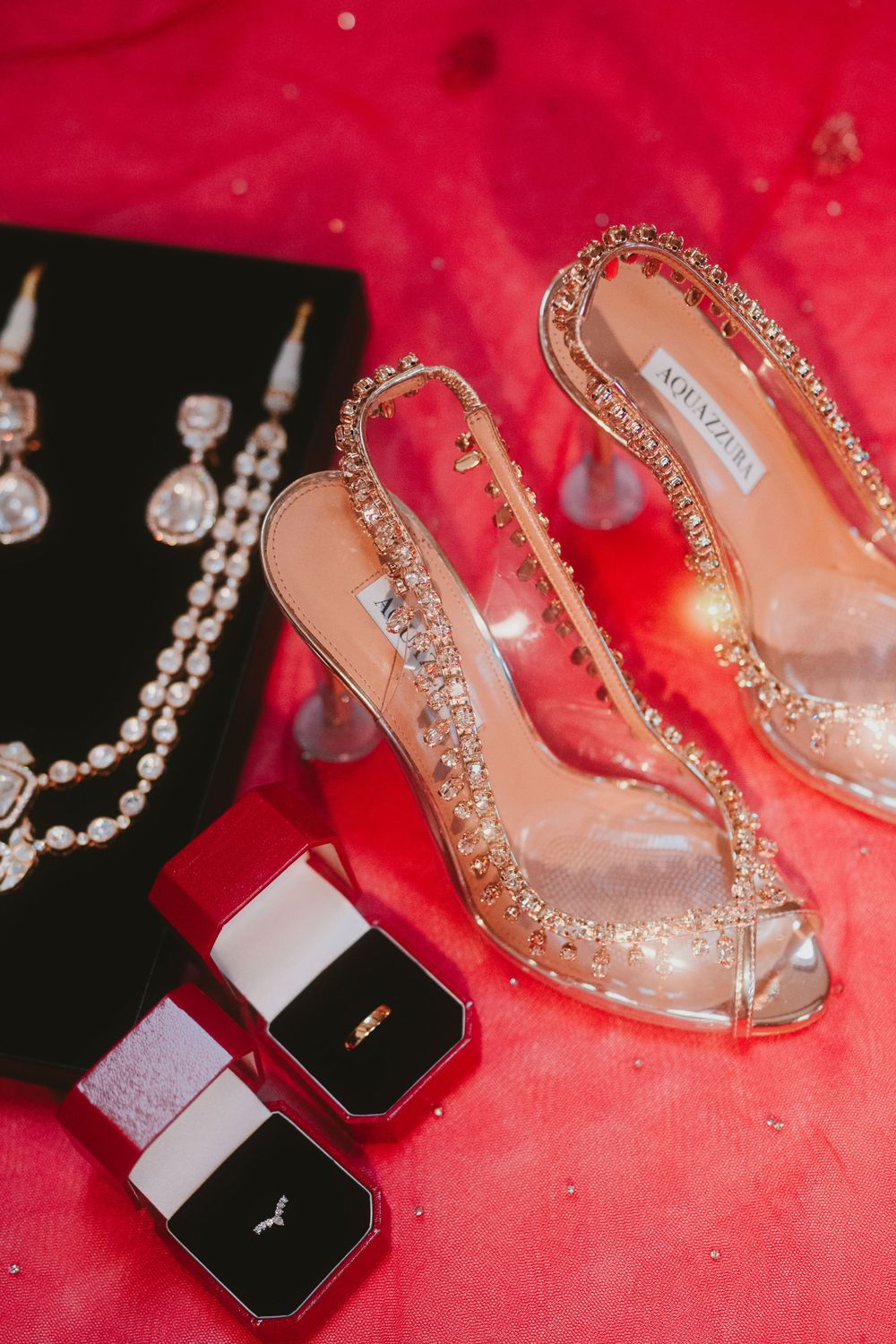 Sparkly bridal shoes and jewelry boxes arranged on red fabric.