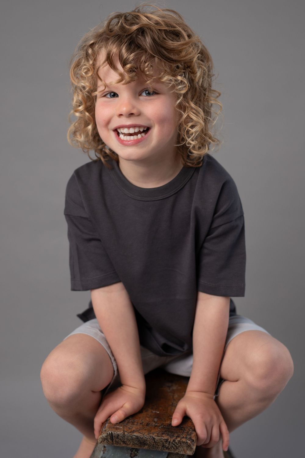 Candid poses of enthusiastic child with curly hair wearing a black t-shirt on gray background.