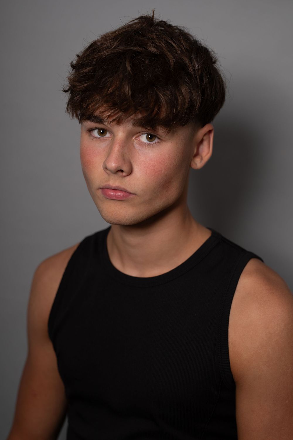 A series of studio portraits showing a person with tousled dark hair wearing a black sleeveless top against a gray background.