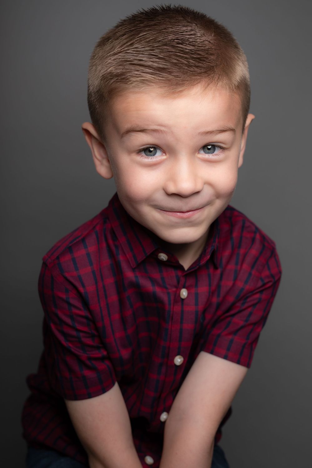 Child wearing red and black plaid button-up shirt poses against dark background with playful expressions.