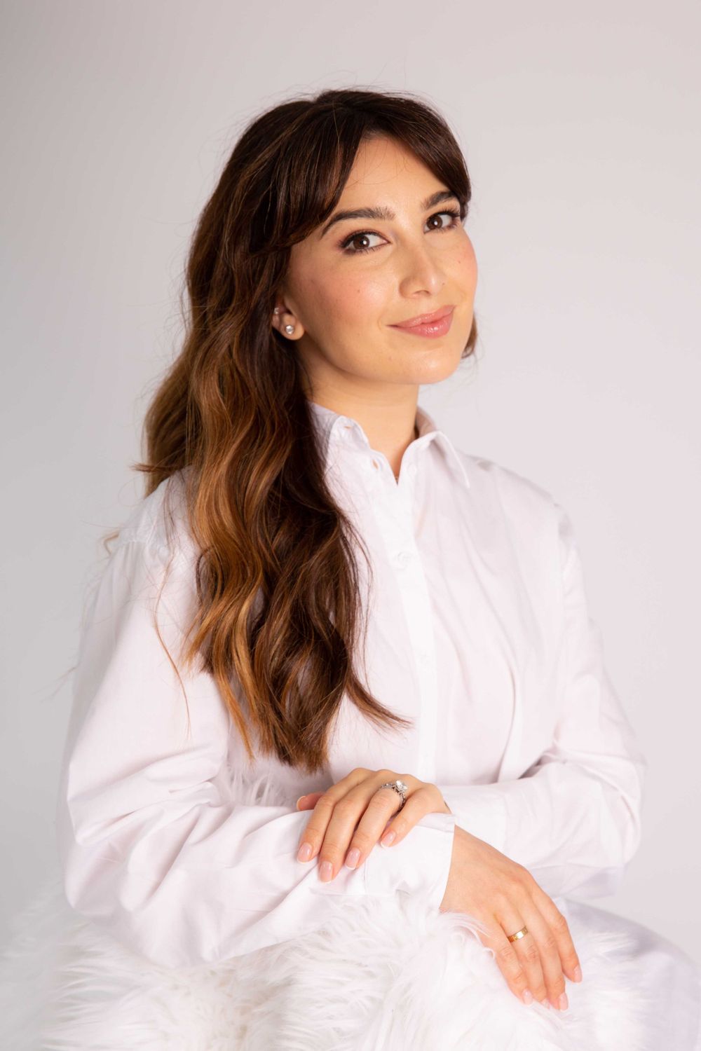 Professional studio portrait of someone wearing a crisp white button-down shirt against a light gray background.