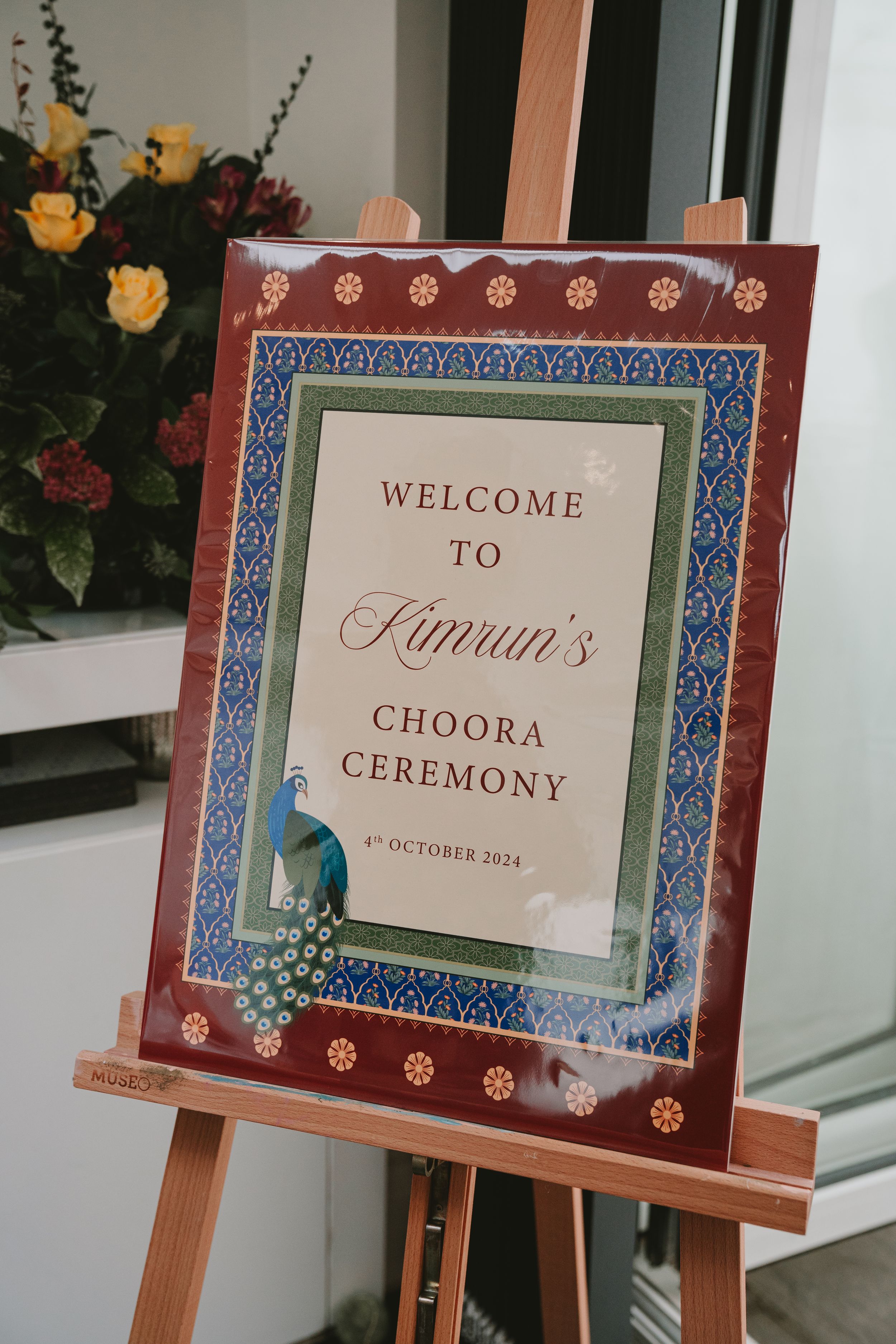 Ornate welcome sign for Simran's Choora Ceremony displayed on wooden easel with floral decorations.