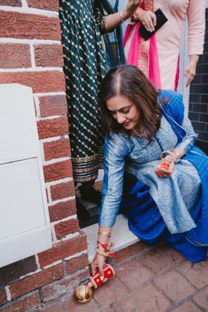 Person in blue traditional dress adjusting decorative footwear at cultural event.