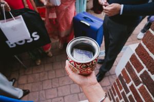Hand holding a decorative metal tumbler with intricate designs during an outdoor gathering.