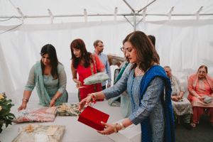 Celebration guests serving food at a buffet table under white tent.