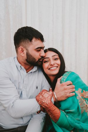 Couple in traditional dress sharing an intimate moment against white background.